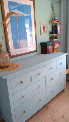 a blue dresser in a room with pictures on the wall and a painting above it