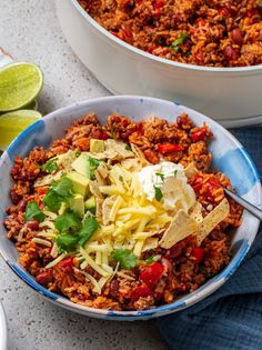 two bowls filled with taco salad and tortilla chips next to limes