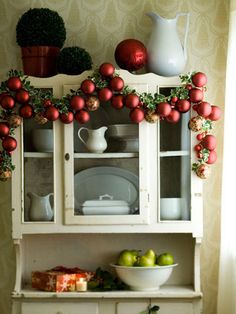 an old china cabinet decorated with christmas decorations and apples on it's top shelf