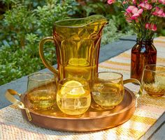 a pitcher and glasses on a tray with flowers in the background