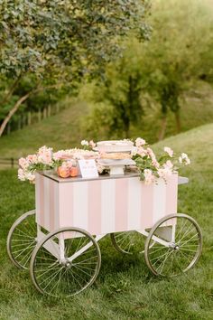 a pink and white striped cart with flowers on the top is sitting in the grass