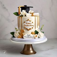 a graduation cake decorated with gold icing and white flowers on a marble table top