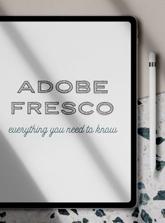 an ipad with the words adobe fresco on it next to a pen and paper