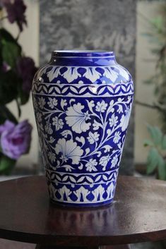 a blue and white vase sitting on top of a wooden table next to purple flowers