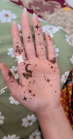 a person's hand with stars and moon tattoos on their palm, in front of a flowery blanket