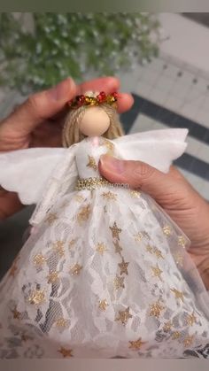 a person holding a doll in their hand with gold and white lace on the bottom