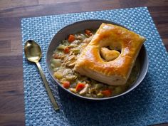 a bowl filled with chicken pot pie on top of a blue place mat next to a spoon