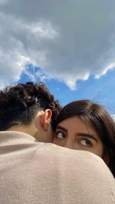 a man and woman embracing each other under a cloudy blue sky