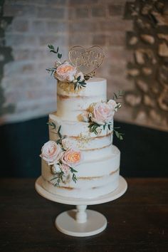 the wedding cake is white and has pink flowers on it, while people are looking at it