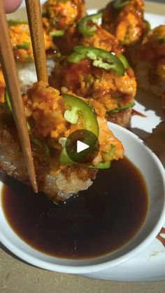 a person holding chopsticks over some food on a white plate with sauce in it