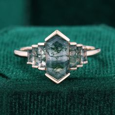 a close up of a ring on a green velvet surface with an emerald colored diamond in the center