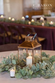 a lantern is sitting on top of a table with greenery and candles in front of it