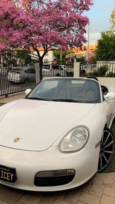 a white sports car parked in front of a fence with pink flowers on the trees