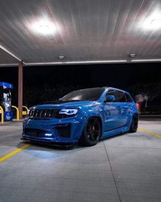 a blue jeep is parked in front of a gas station at night with its lights on