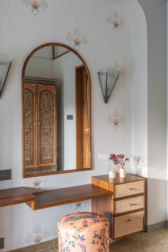 an ornate mirror hangs on the wall above a dressing table with stool and footstool