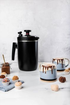 an ice cream dessert is being served in front of a coffee pot and cupcakes