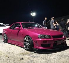 a pink car parked in front of a group of people