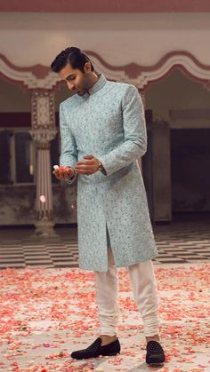 a man in a blue sherwa with white pants and black shoes looking at his phone