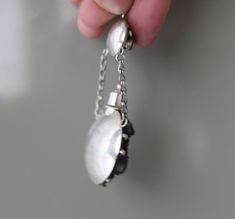 a hand holding a chain with a white pearl on it and a black bead around the end