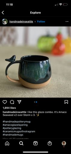 a black ceramic cup with a bird on it's handle is sitting on a table