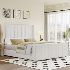 a white bed sitting in a bedroom on top of a hard wood floor next to a window