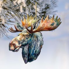 a moose ornament hanging from a tree branch with snow on it's branches