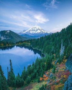 a lake surrounded by trees with a snow capped mountain in the background and blue sky