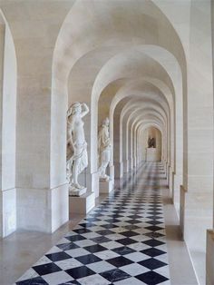 the hallway is lined with marble statues and black and white checkered flooring