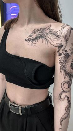 a woman with a dragon tattoo on her arm and shoulder, standing in front of a wall