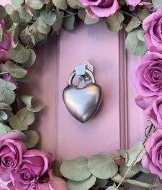 a heart shaped metal object sitting on top of a purple door surrounded by flowers and greenery