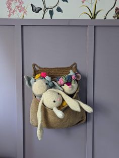 two stuffed animals are in a bag hanging on the side of a purple painted wall