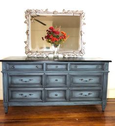 a blue dresser with flowers and a mirror on top