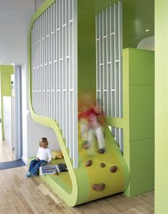 two children playing on a climbing wall in a playroom with green walls and white slats