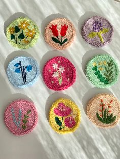 nine crocheted flower coasters are arranged on a white tablecloth, each with different designs and colors