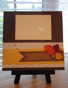 an easel is decorated with fall leaves and a photo frame on top of it