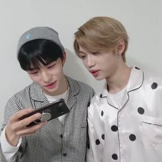 two young men standing next to each other looking at a cell phone