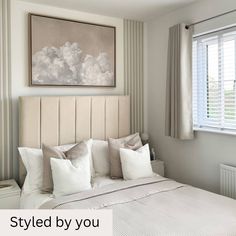 a bedroom with white bedding and pillows on the headboard, framed art above the bed