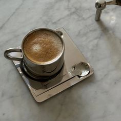 a cup of coffee sitting on top of a metal tray next to a faucet