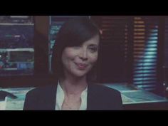 a woman in a black jacket is smiling at the camera while she sits in front of a computer desk