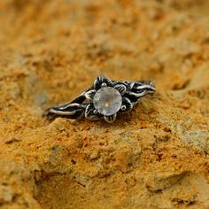 a silver ring with a stone in the middle on top of some sand and dirt