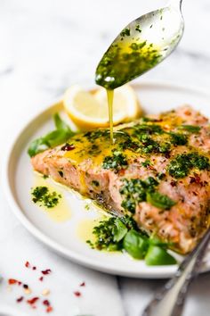 a piece of salmon being drizzled with olive oil on a white plate