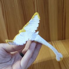 a hand is holding a small white and yellow bird ornament on a wooden surface