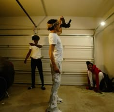 three people standing in a garage with one person holding something up to the ceiling and another man sitting on the floor