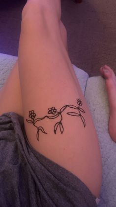 a woman's leg with a tattoo on it that has flowers and leaves drawn on it