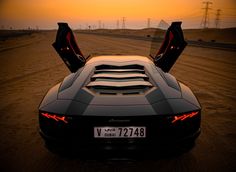 a black sports car with its doors open in the middle of an empty road at sunset