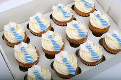 twelve cupcakes with blue and white frosting in a box on a table