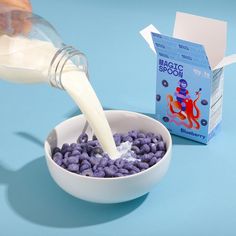 a person pouring milk into a bowl filled with blueberries next to a carton of milk