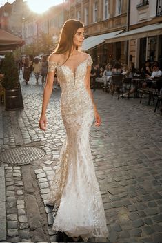 a woman in a wedding dress walking down the street with people sitting at tables behind her