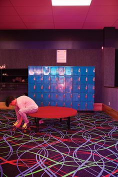 a man kneeling down on top of a red table in front of a blue locker