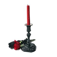 a single red candle sitting on top of a black stand next to a dead rose